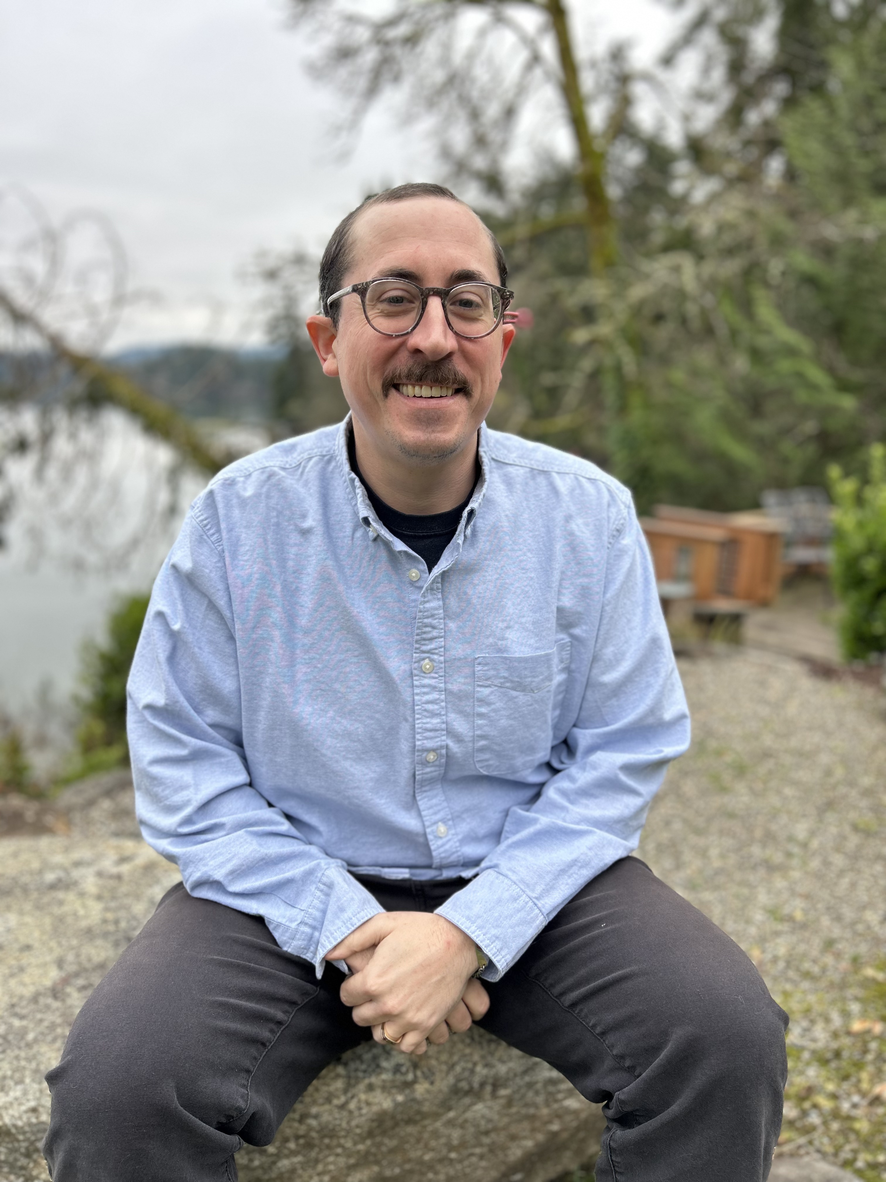 A photo of Maximo, smiling, and sitting on a rock. 